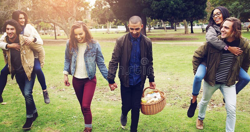 Glada vänner och att hålla händer med picknickkorgen i parken för att knyta samman eller socialt samlas i naturen. par royaltyfri bild