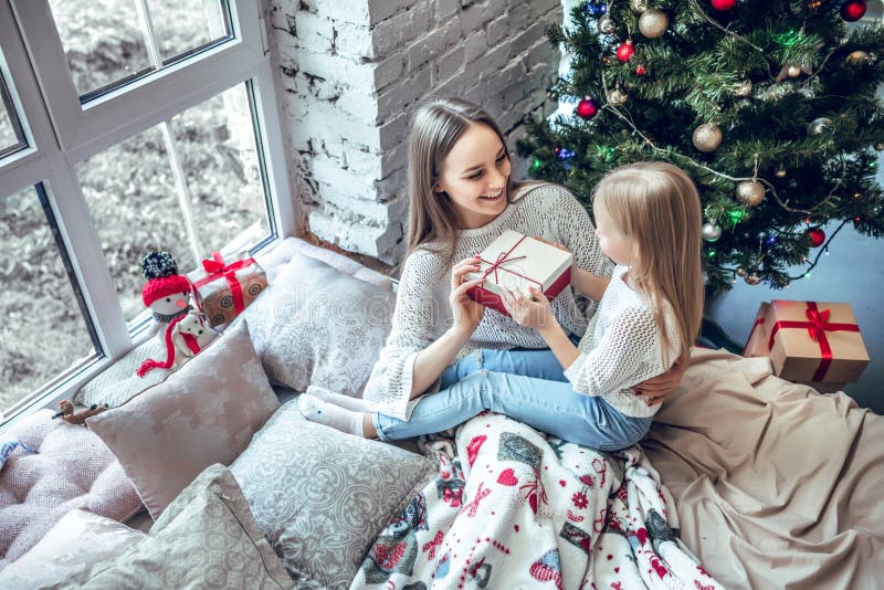 Gladlynt mamma och hennes gullig dotterflicka som utbyter gåvor nära fönster royaltyfri foto