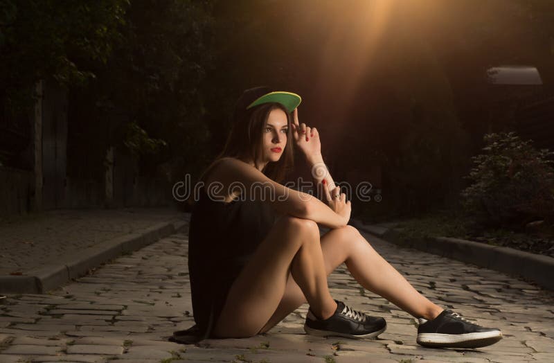 Glamor brunette girl in sport apparel sitting on the cobbles at