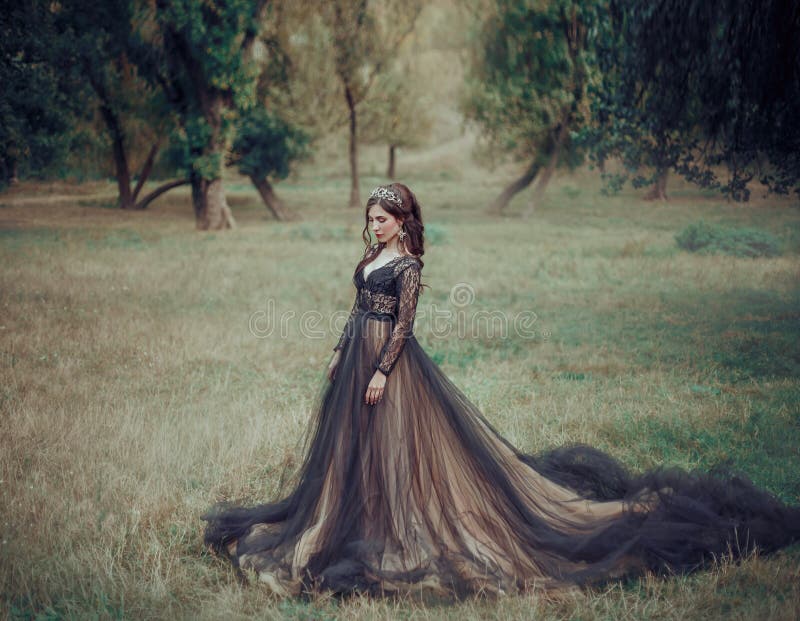 Glamorous fashion woman in luxurious black dress with beige long train. Backdrop summer nature. Gothic fantasy beauty