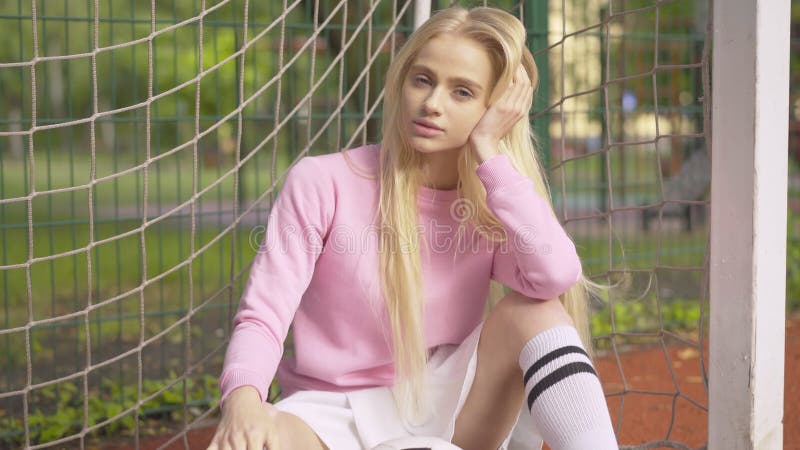 Glamouröse junge blonde Frau, die mit Fußballball auf Sportplatz im Freien sitzt. Kameraansätze an schönen Kaukasier stock footage