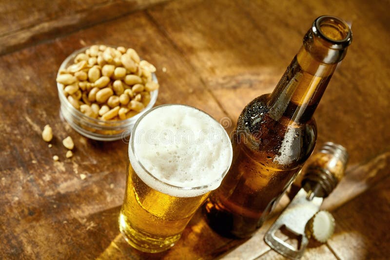 Glas Bier op Lijst met Opener en Pinda's royalty-vrije stock afbeelding Glas Bier op Lijst met Opener en Pinda's royalty-vrije stock afbeelding
