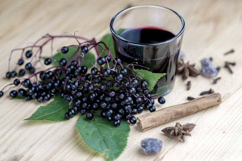 Glass of fresh elderberry syrup with cinnamon stick, brown sugar, star anise and elderberries on a wooden kitchen counter. Glass of fresh elderberry syrup with cinnamon stick, brown sugar, star anise and elderberries on a wooden kitchen counter