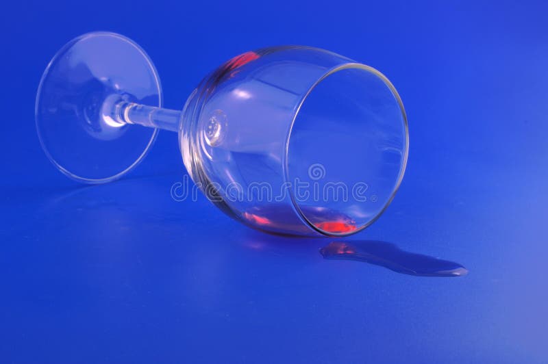 Inverted glass with the residue of red wine spilled on a blue background. Inverted glass with the residue of red wine spilled on a blue background