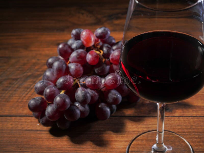 Glas Rotwein in der Fokusgruppe von frischen roten Trauben auf einem Holztisch aus Draufsicht Fokus heraus stockfotografie