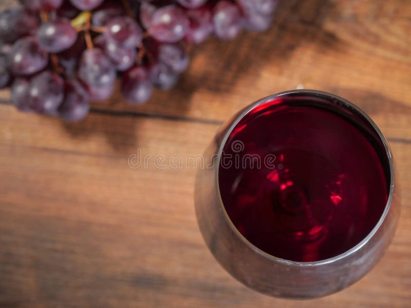 Glas Rotwein im Fokus Gruppe von frischen roten Trauben auf einem Holztisch unscharf, Draufsicht stockbild