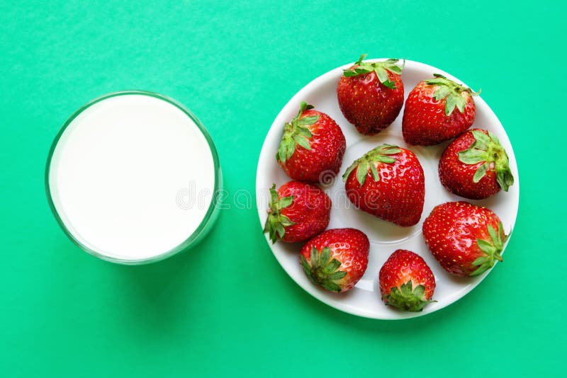 Glas von Milch und von weißer Untertasse mit reifer roter Erdbeere auf einem Türkishintergrund, Draufsicht lizenzfreie stockfotos Glas von Milch und von weißer Untertasse mit reifer roter Erdbeere auf einem Türkishintergrund, Draufsicht lizenzfreie stockfotos