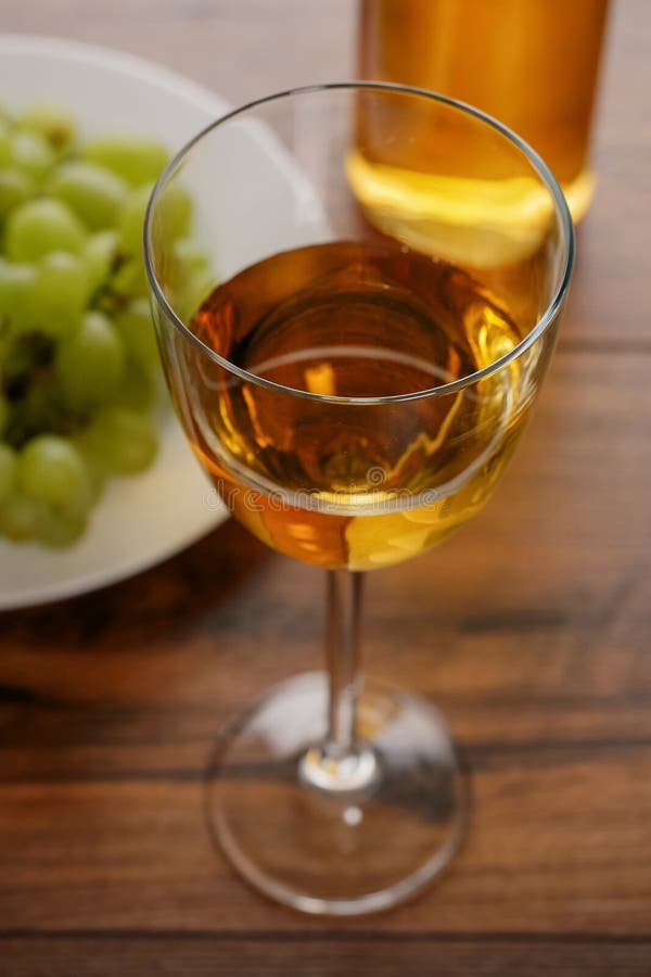 Glas Weißwein in der Fokusgruppe aus frischen Weintrauben auf einer weißen Jury und einer Flasche Wein unscharf. Dunkle Holz talbe stockfotografie