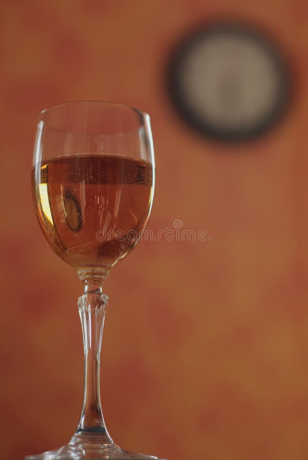 Glass of white wine on a background with a blurred image of a clock. Alcohol can make you disoriented and can make you losing the sense of time. Glass of white wine on a background with a blurred image of a clock. Alcohol can make you disoriented and can make you losing the sense of time.
