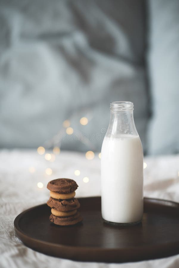 Glasflasche mit frischer Milch und Stapel von Schokoladenkeksen auf Holztablett in Bettschließung. leckeres Frühstück. Guten Morge