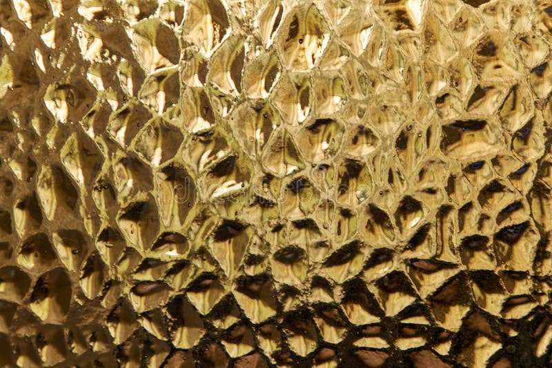 Glass product made of painted with gold paint. The surface of the glass with recesses in the form of diamonds. Looks like a piece of gold bullion. Symbol of wealth. Background or texture. Glass product made of painted with gold paint. The surface of the glass with recesses in the form of diamonds. Looks like a piece of gold bullion. Symbol of wealth. Background or texture.