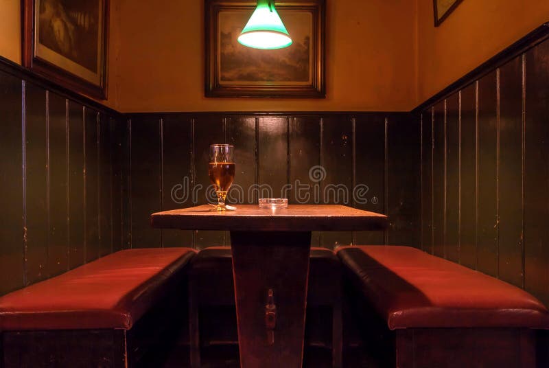 Glass of beer on wooden table of historical bar of danish capital with dark retro decoration