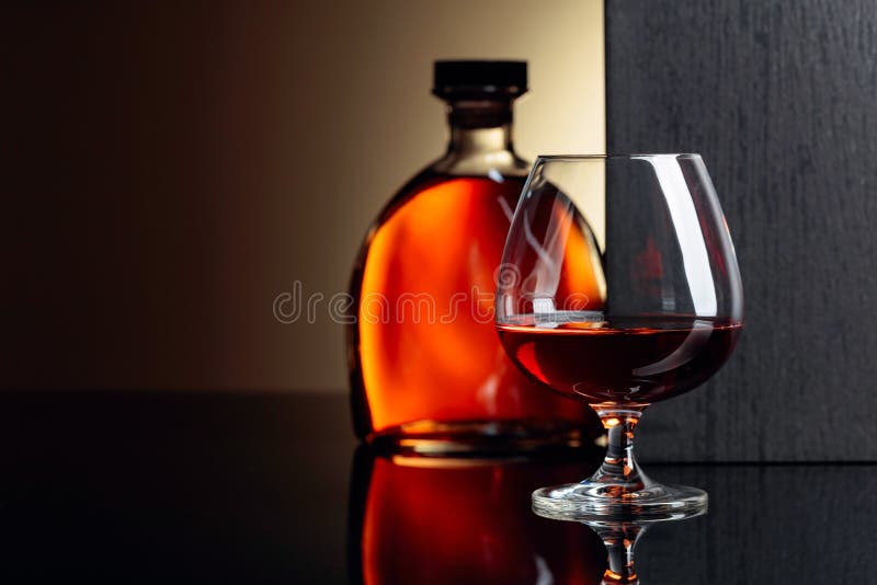 Glass and bottle of brandy on a black reflective background