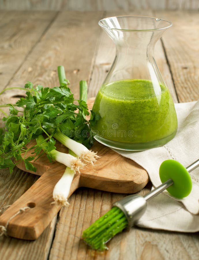 Glass bottle of green olive oil and green onion with parsley