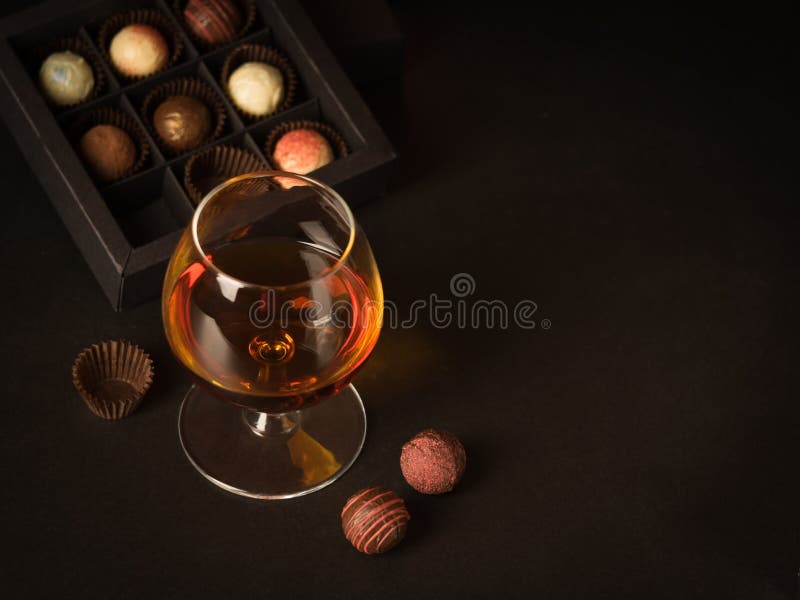 A glass of brandy and chocolate candy on a dark background. Alcoholic drink and elite chocolate food concept.