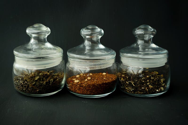 Glass clear jars round bellied low for tea with lid on black textured background with custard black and green tea inside stock photos