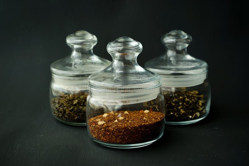 Glass clear jars round bellied low for tea with lid on black textured background with custard black and green tea inside royalty free stock image