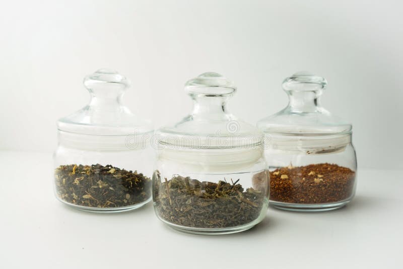 Glass clear jars round bellied low for tea with lid on white background with custard black and green tea inside royalty free stock photo.
