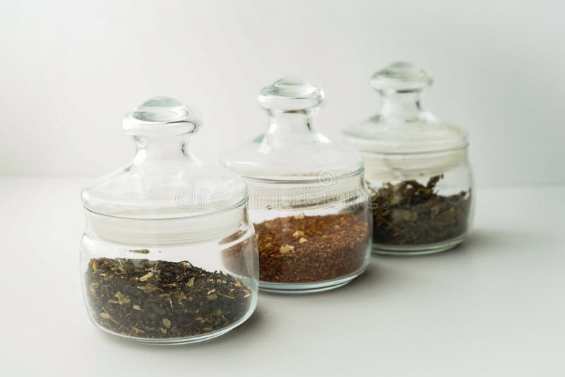 Glass clear jars round bellied low for tea with lid on white background with custard black and green tea inside stock images