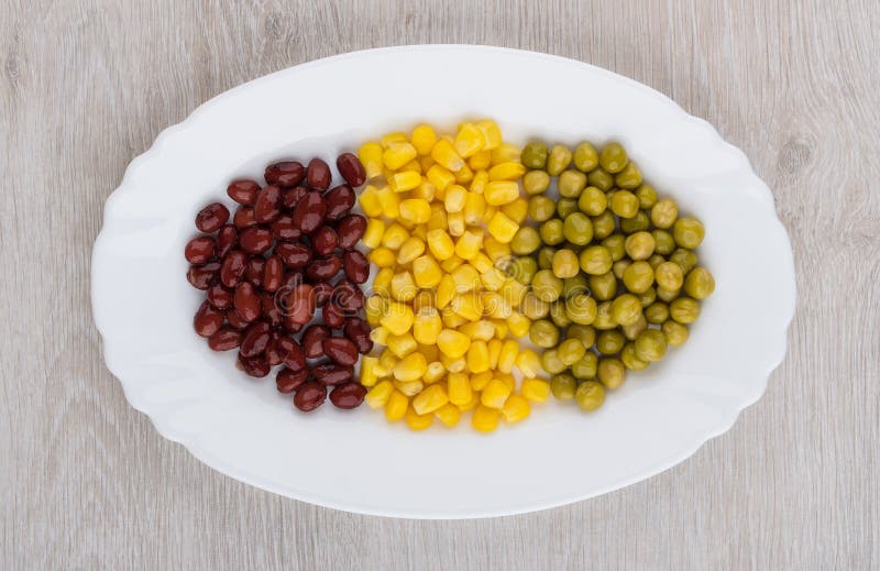 Glass dish with green peas, beans, sweet corn on table