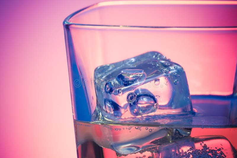 Glass of drink with ice on disco violet light