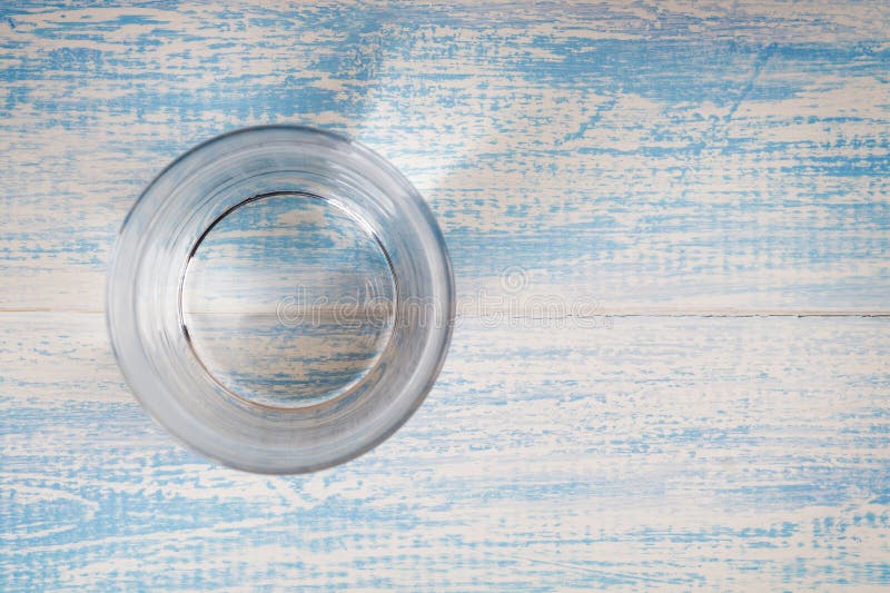 Glass of drinking water on a blue wooden background top view. Freash water cup overhead