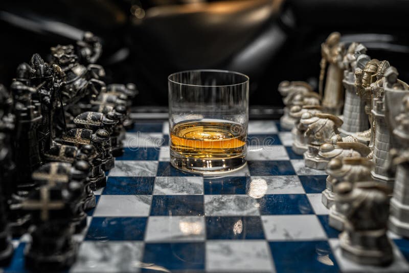 Focused man sipping alcoholic beverage while thinking about next chess move.  Stock Photo by DC_Studio