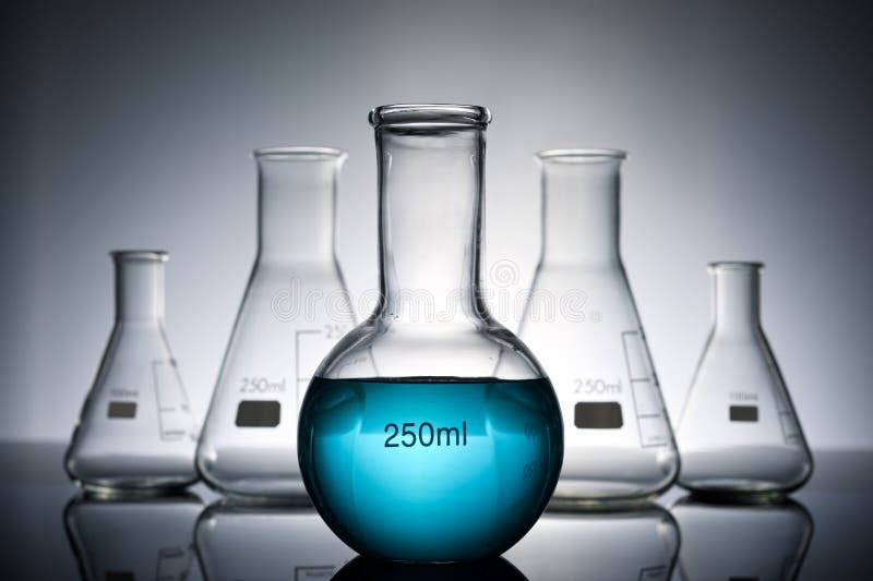 Glass flasks placed in a laboratory table with blue liquid stock images