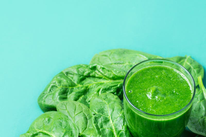 Glass with Green Fresh Smoothie from Leafy Greens Vegetables Fruits. Apples Bananas Kiwi Zucchini Scattered Spinach Leaves