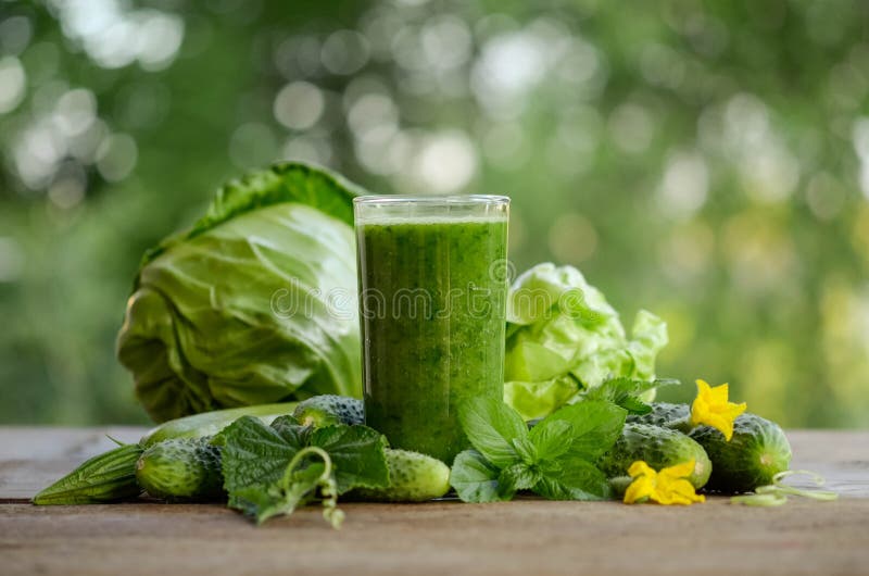 Glass with green smoothie on a wooden table and vegetables