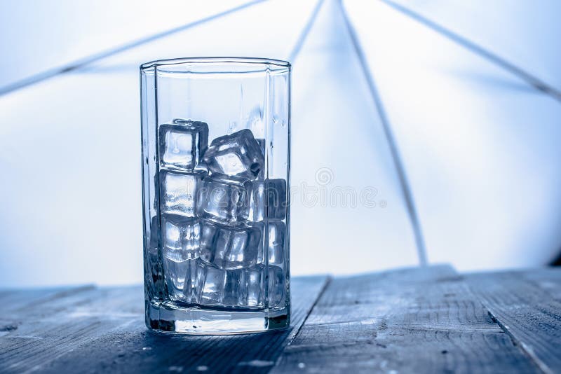 Glass of Ice cube on blue wooden table background.