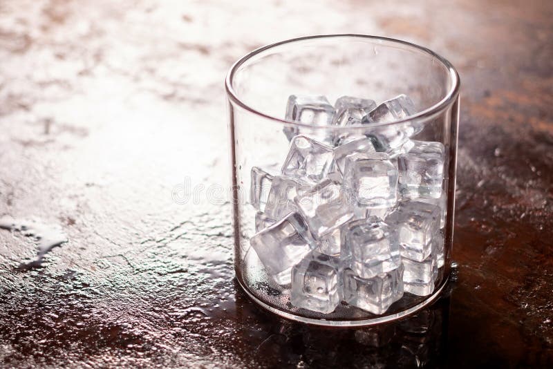 Glass of Ice cube on wooden table and light blurred background