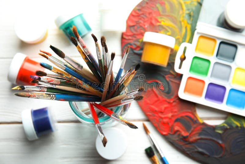 Glass jar with brushes, paints and palette on wooden background