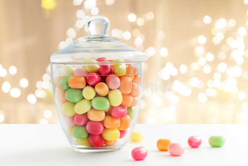 Glass jar with candy drops over lights background