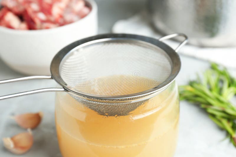 Glass Jar with Delicious Bone Broth and Sieve on Table, Closeup Stock