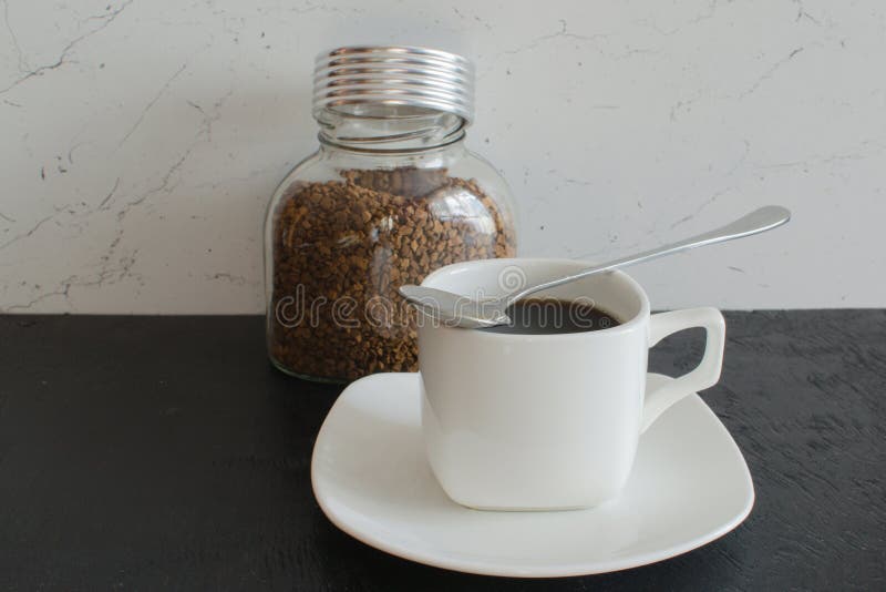 A Glass Jar of Instant Coffee in Large Granules Next To a White Mug