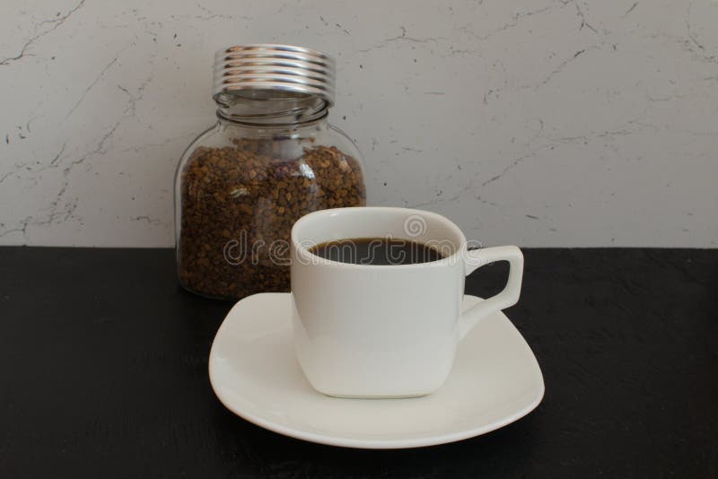 A Glass Jar of Instant Coffee in Large Granules Next To a White Mug