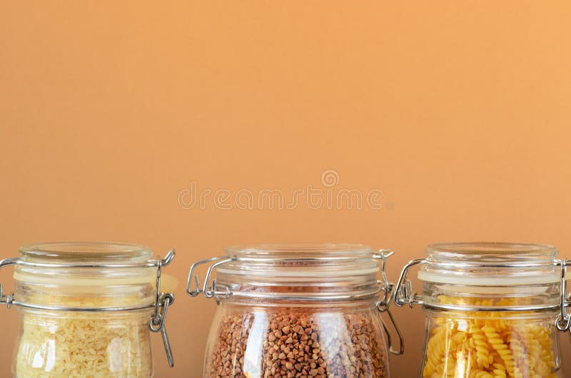 Glass jars with uncooked cereals, pasta, rice, buckwheat on a beige background. Zero waste concept, housewares