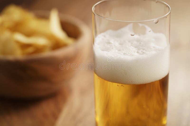 Glass of lager beer with potato chips on wooden table