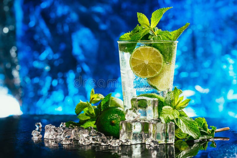 Glass of mojito with lime and mint ice cube close-up red straw on blue background