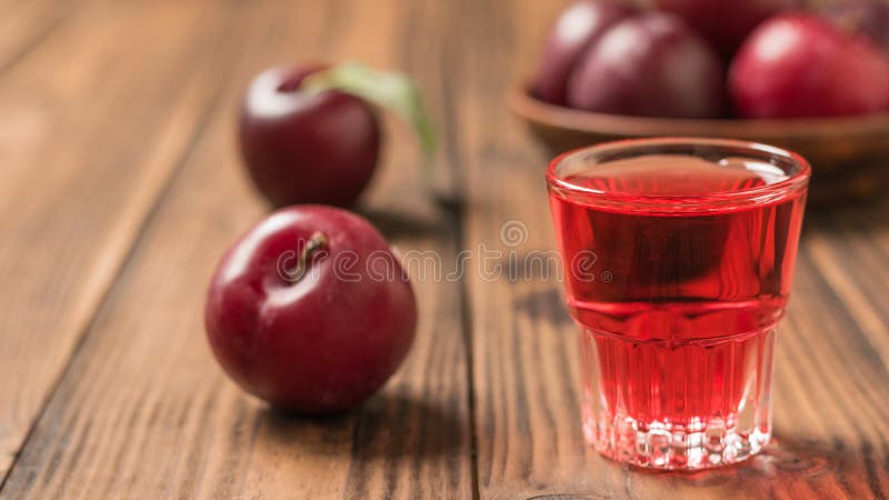 A glass of plum liqueur with a bowl of plums on a wooden table stock photography A glass of plum liqueur with a bowl of plums on a wooden table stock photography
