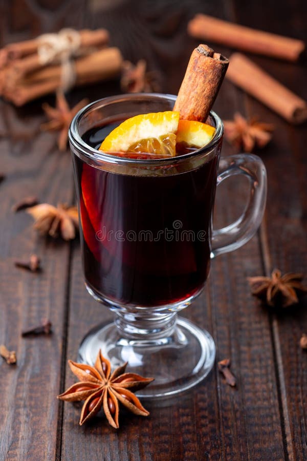 Glass of red glogg or mulled wine with orange slices and cinnamon stick on dark wooden background, vertical