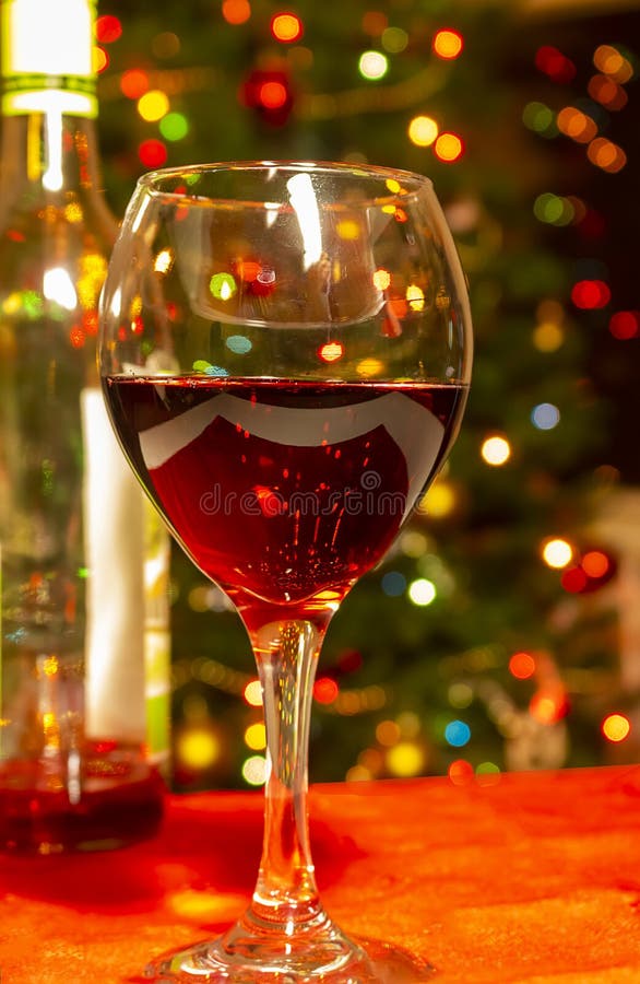 Glass of red wine and wine bottle in front of bokeh Christmas tree. Glass of red wine and wine bottle in front of bokeh Christmas tree.