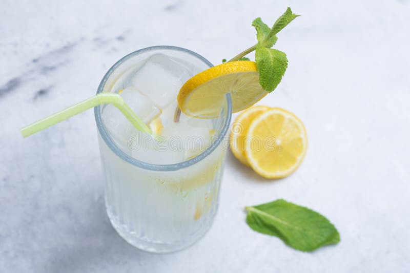 A glass of refreshing lemon water with ice cubes, mint leaves and a straw stands on a light marble background. A citrus drink for royalty free stock photo