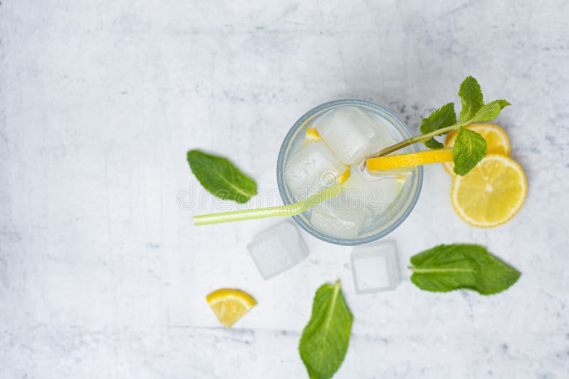 A glass of refreshing lemon water with ice cubes, mint leaves and a straw stands on a light marble background. A citrus drink for royalty free stock photos
