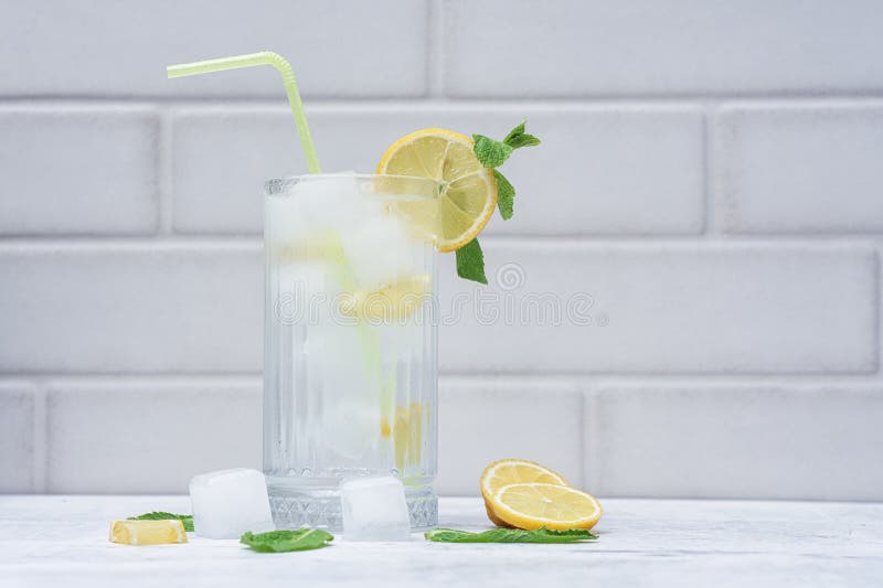 A glass of refreshing lemon water with ice cubes, mint leaves and a straw stands on a light marble background. A citrus drink for royalty free stock photo