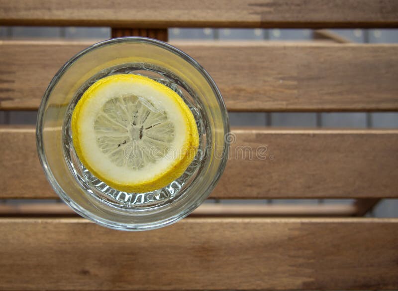 A glass of refreshing water with lemon on a wooden table. Garden furniture on the terrace of a country house. Horizontal orientati stock image A glass of refreshing water with lemon on a wooden table. Garden furniture on the terrace of a country house. Horizontal orientati stock image