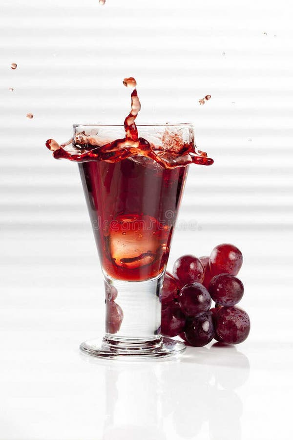 glass with splashing red grape juice, close up.