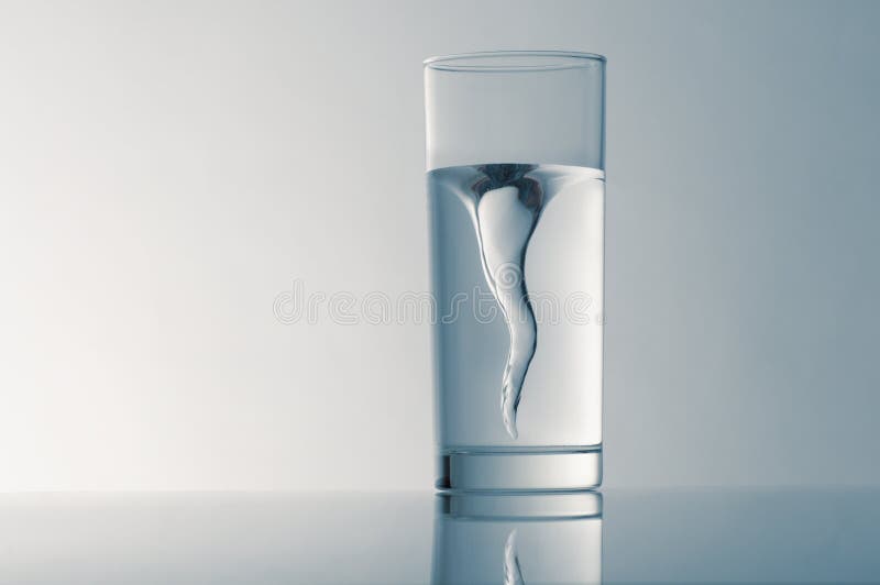 Glass with spring water against a blue background. Whirlpool vortex water stock images, royalty-free photos and pictures