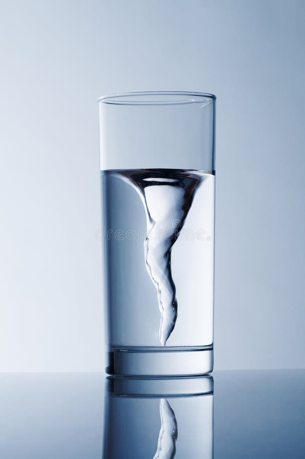 Glass with spring water against a blue background. Whirlpool vortex water stock images, royalty-free photos and pictures